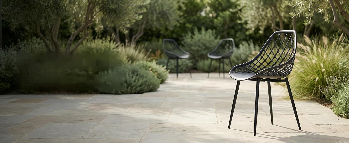 Terrasse extérieure moderne avec chaise en métal noir au design incurvé positionnée sur une terrasse en béton gris clair entourée d'un jardin paysager avec des herbes et des arbustes ornementaux.