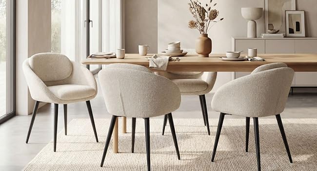 Ensemble de salle à manger moderne comprenant une table ronde en bois et quatre chaises beiges rembourrées aux pieds noirs dans un espace intérieur contemporain avec étagères et éclairage naturel.