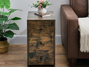 Rustic wooden nightstand with three drawers beside a brown leather armchair. Decorated with a plant, flower vase, and book on top.