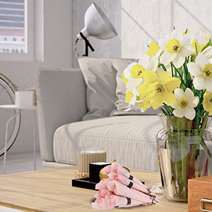 Living room corner with beige sofa, wooden coffee table, yellow daffodils in glass vase, and pink accessories on table.