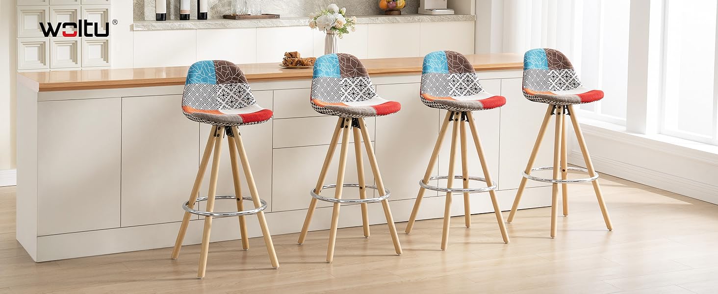 Cuatro taburetes de bar tapizados en patchwork con patas de madera en un entorno de cocina. Los asientos tienen patrones azules, negros y blancos con detalles en rojo. Los taburetes tienen un diseño moderno y ecléctico