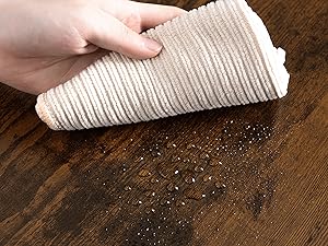 Tieni a mano un panno bianco a coste o un tovagliolo di carta su una superficie di legno, con detriti o briciole visibili