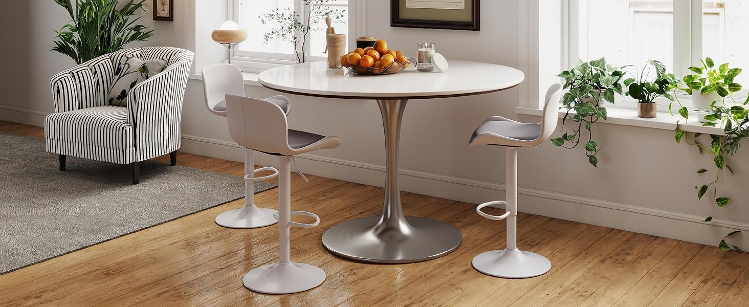 Modern dining area setup with white pedestal table and chairs, featuring decorative plants and food presentation in contemporary interior setting.