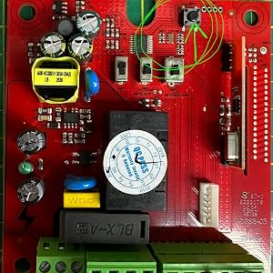 Close-up view of red circuit board featuring integrated circuits, capacitors, and screw terminals with black and green connector blocks.