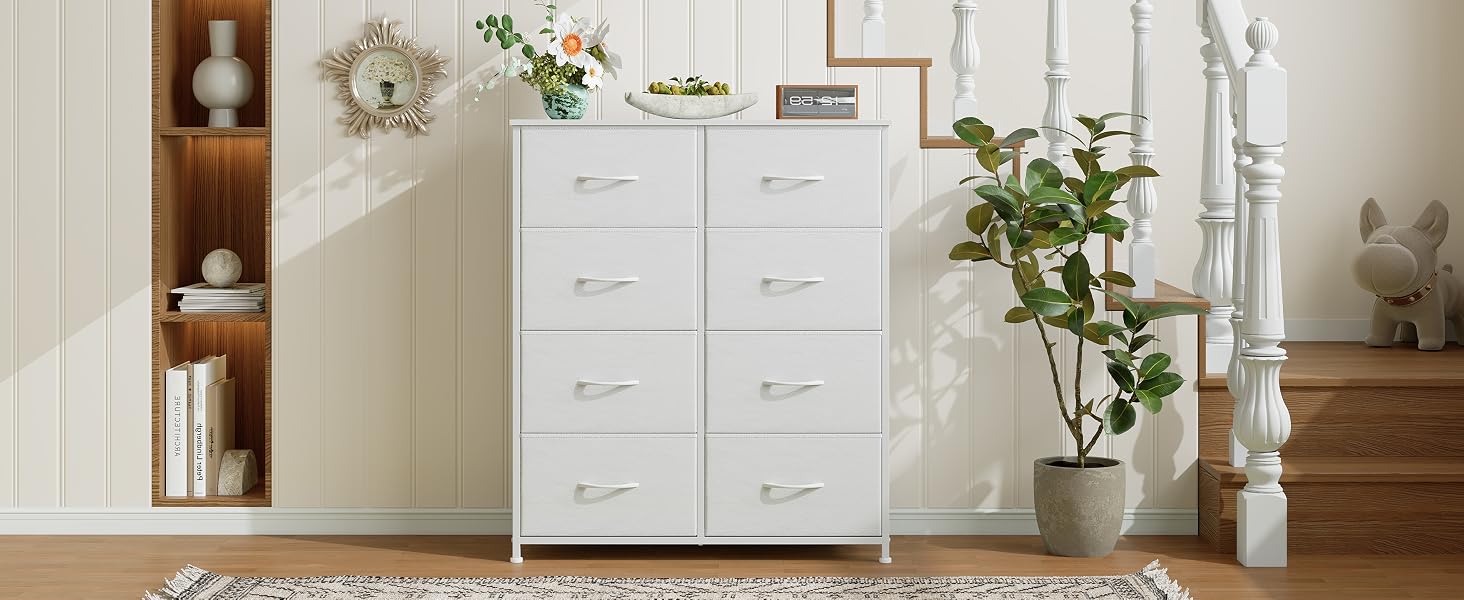 Commode en bois blanc à huit tiroirs dans un décor de chambre à coucher. Entouré d'objets décoratifs tels que des plantes, des vases et des œuvres d'art mural, il crée une scène de décoration intérieure cohérente