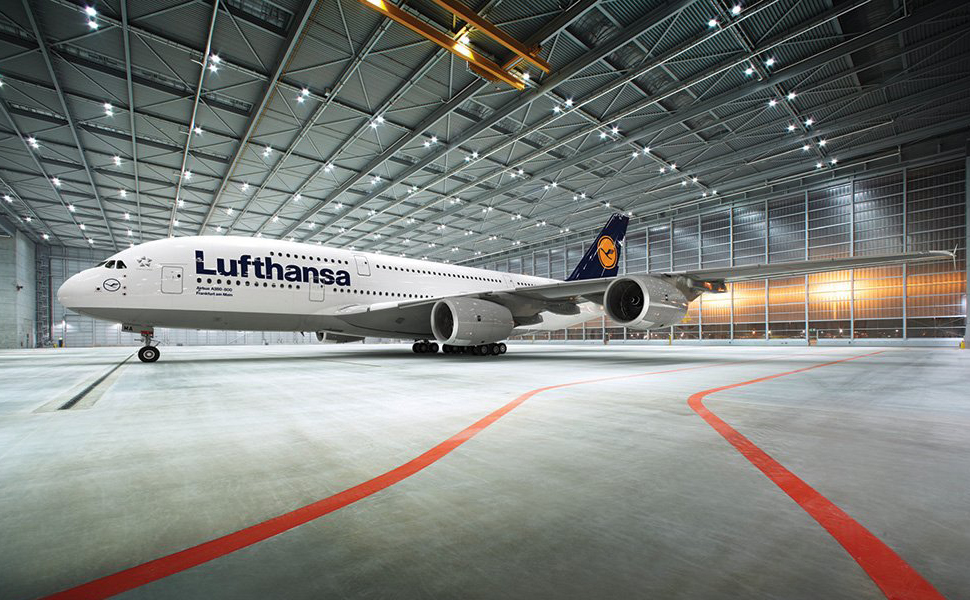 Lufthansa-Flugzeug im Hangar mit hoher Decke. Großes weißes Flugzeug mit blauem Hecklogo auf grauem Boden mit roten Leitlinien