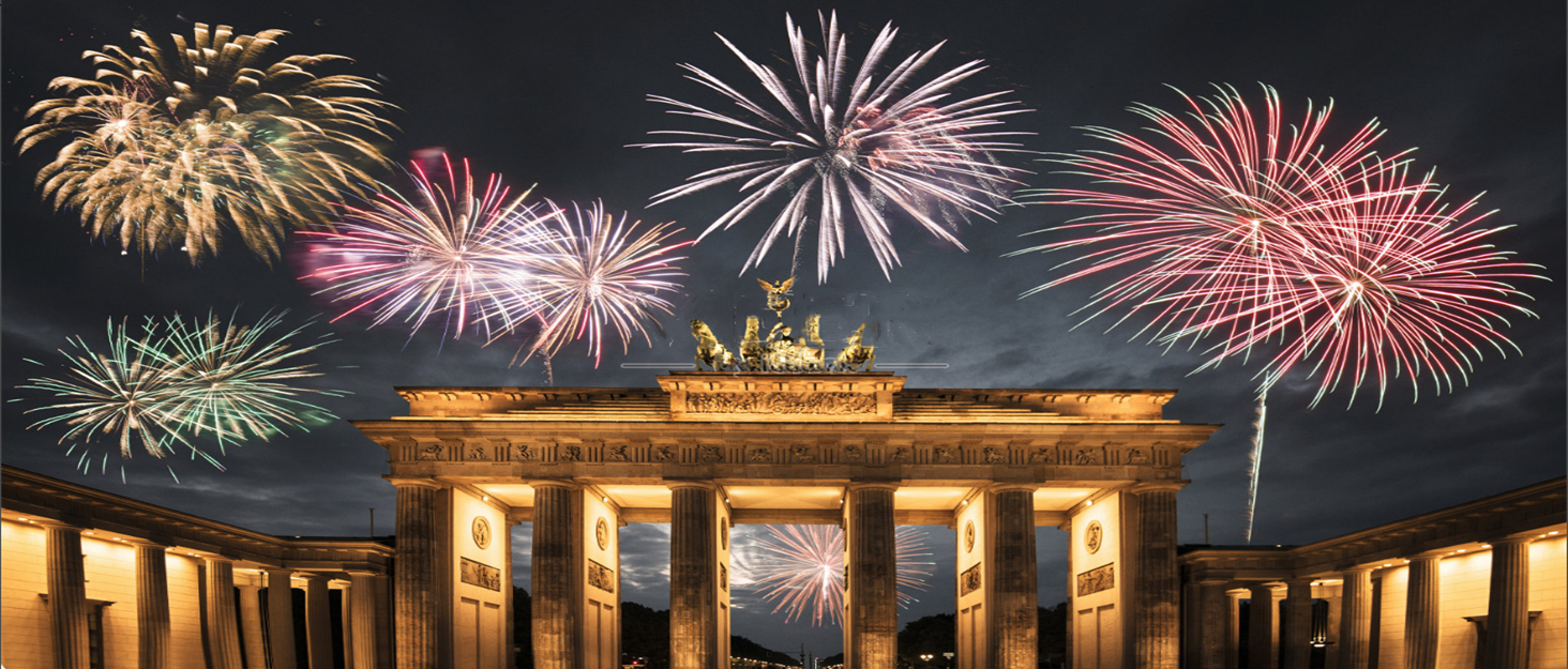 Fireworks exploding over the Brandenburg Gate at night, illuminating the sky with colorful bursts of light against the iconic landmark.