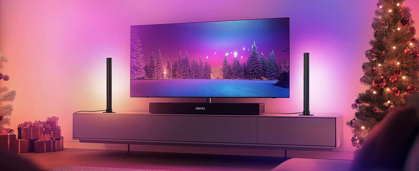 Großer Flachbildfernseher mit Winterszenen, montiert über der Soundbar auf einem weißen Gehäuse. Flankiert von zwei dünnen vertikalen Lichtern. Weihnachtsbaum und Geschenke sichtbar, mit violetter Umgebungsbeleuchtung