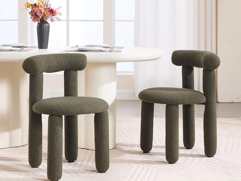 Two modern sculptural dining chairs with rounded forms, upholstered in dark textured fabric, positioned in bright white room with dining table and floral arrangement.