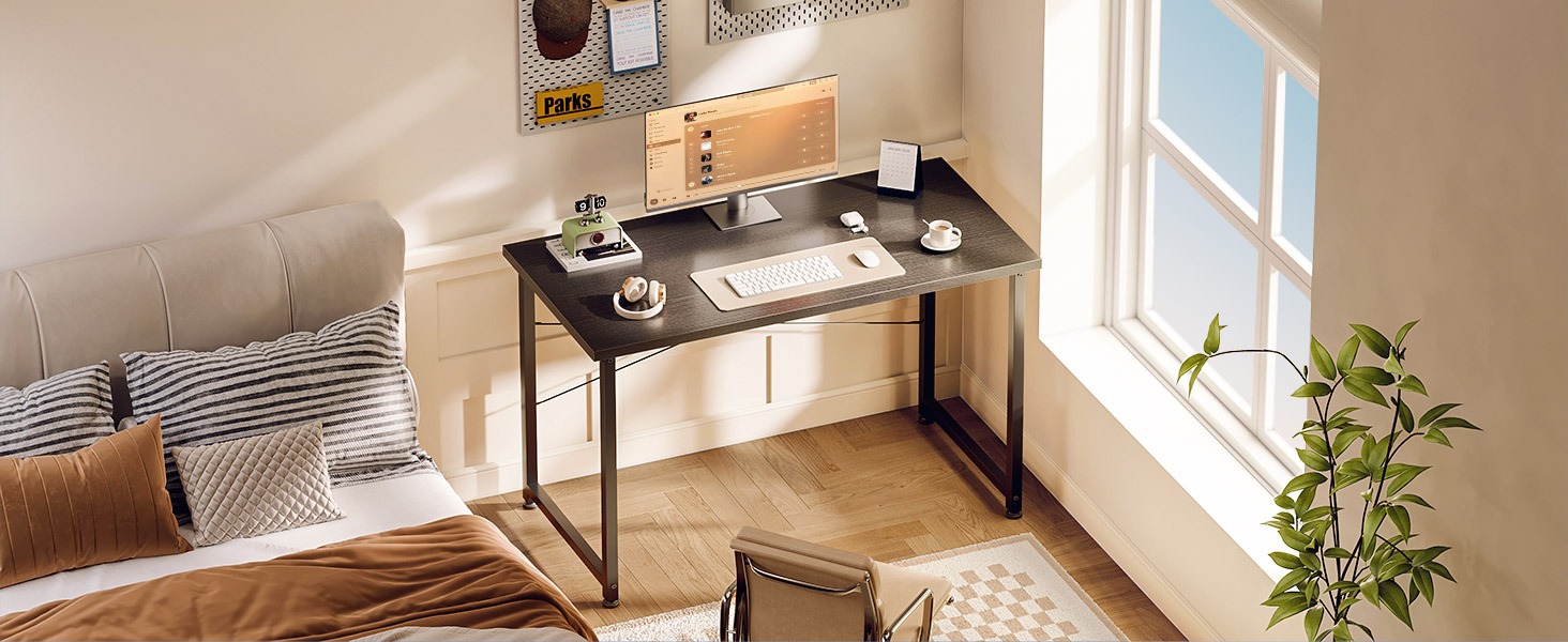 Configuration de bureau à domicile moderne avec bureau en bois foncé contre mur beige, avec écran à double écran. La chambre comprend un lit avec une literie neutre et des coussins décoratifs, ainsi que la lumière naturelle provenant de la fenêtre avec des plantes.