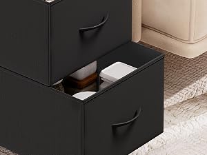 Meuble de rangement noir avec compartiment coulissant ouvert, montrant un espace de rangement intérieur avec des séparateurs blancs et un tapis tissé visible à côté.