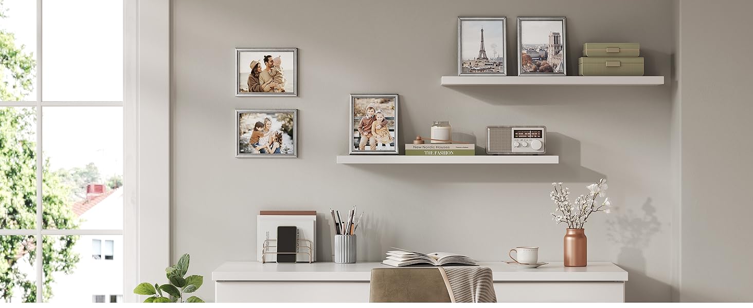 Interno moderno del soggiorno con pareti bianche, mensole galleggianti con cornici e oggetti decorativi e illuminazione naturale dalle finestre.