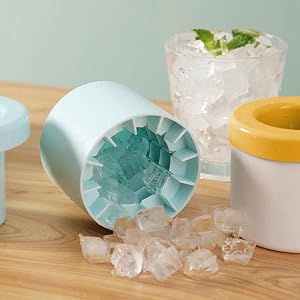 Des bacs à glaçons en silicone de couleur pastel avec de la glace pilée, accompagnés d'un verre d'eau glacée sur une surface en bois