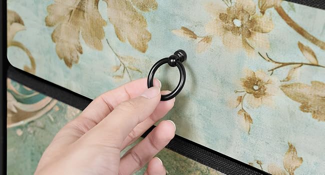 Handdemonstration der Verwendung eines kleinen schwarzen Gardinenrings an einer Stange vor einem Hintergrund mit Blumenmuster. Der Ring verfügt über ein scharniertes Design zum einfachen Anbringen