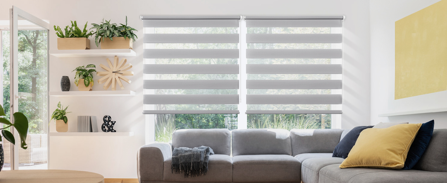 Stores horizontaux gris couvrant de grandes fenêtres dans un salon moderne avec des murs blancs, des plantes et un canapé gris aux accents jaunes.