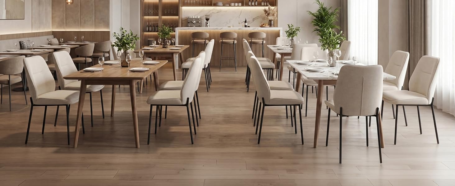 Sala da pranzo moderna con tavolo in legno, sedie imbottite beige con gambe in metallo, illuminazione a sospensione, scaffali con decorazioni e piante in vaso su caldi pavimenti in legno.