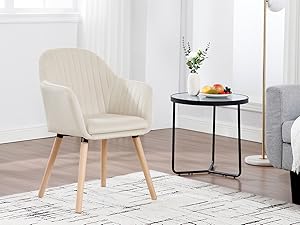 de color crema con respaldo acolchado en forma de canal, brazos curvos y patas de madera, que se muestra junto a una mesa auxiliar redonda negra