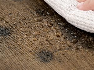 Close-up of water droplets on a brown wooden surface, with a white cloth partially visible in the corner.