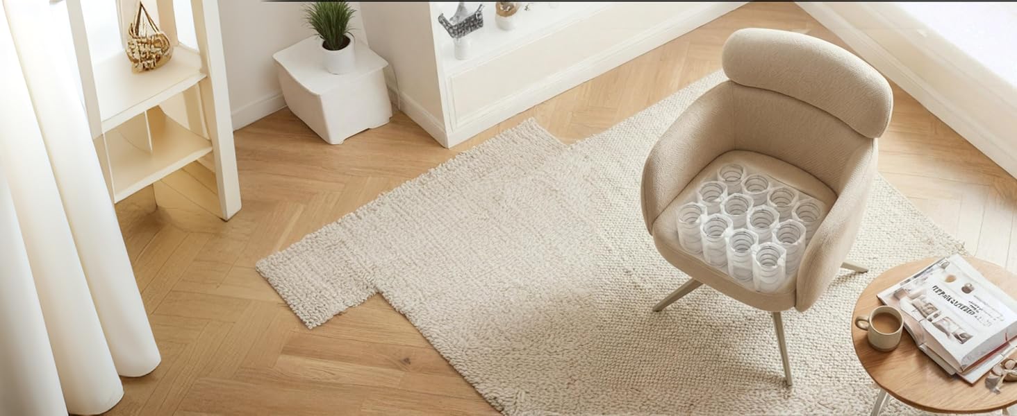 Fauteuil d'appoint rembourré beige placé dans une pièce intérieure de couleur crème avec parquet, rideaux blancs et petits objets décoratifs sur une table d'appoint à côté de la chaise.