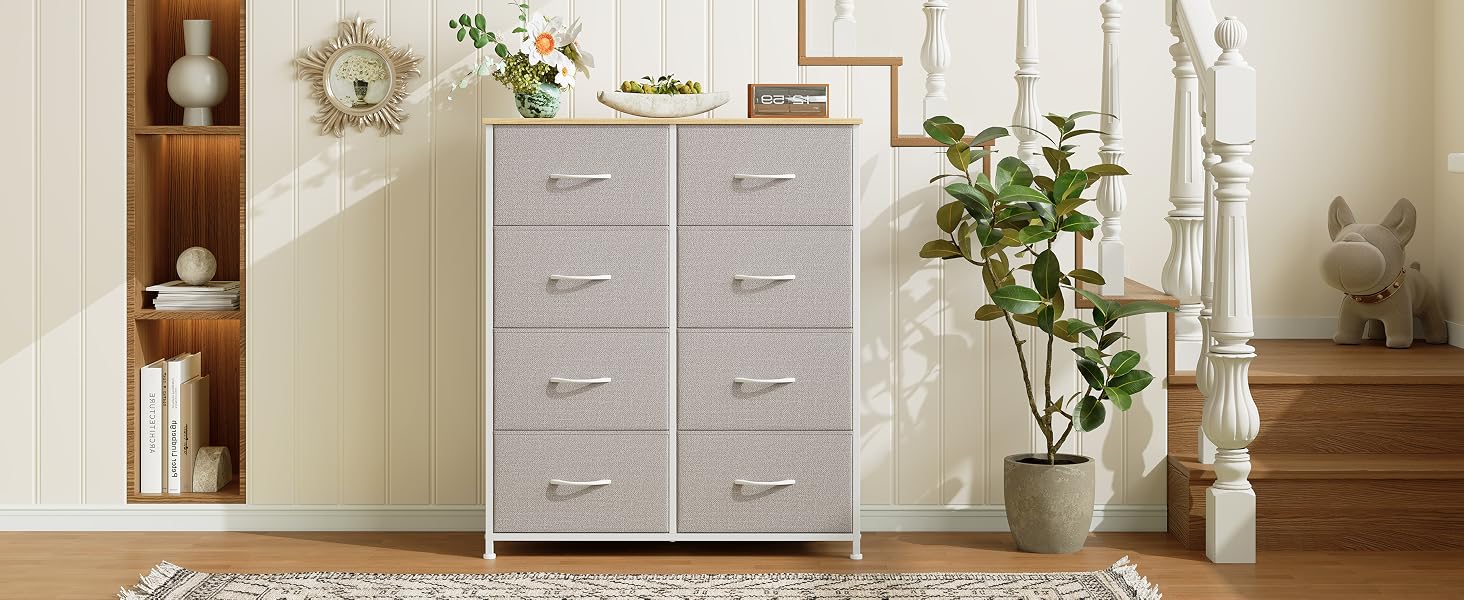 Une commode à six tiroirs avec des tiroirs recouverts de tissu gris clair et un cadre blanc. Situé dans un cadre familial avec des étagères en bois et des éléments décoratifs à proximité