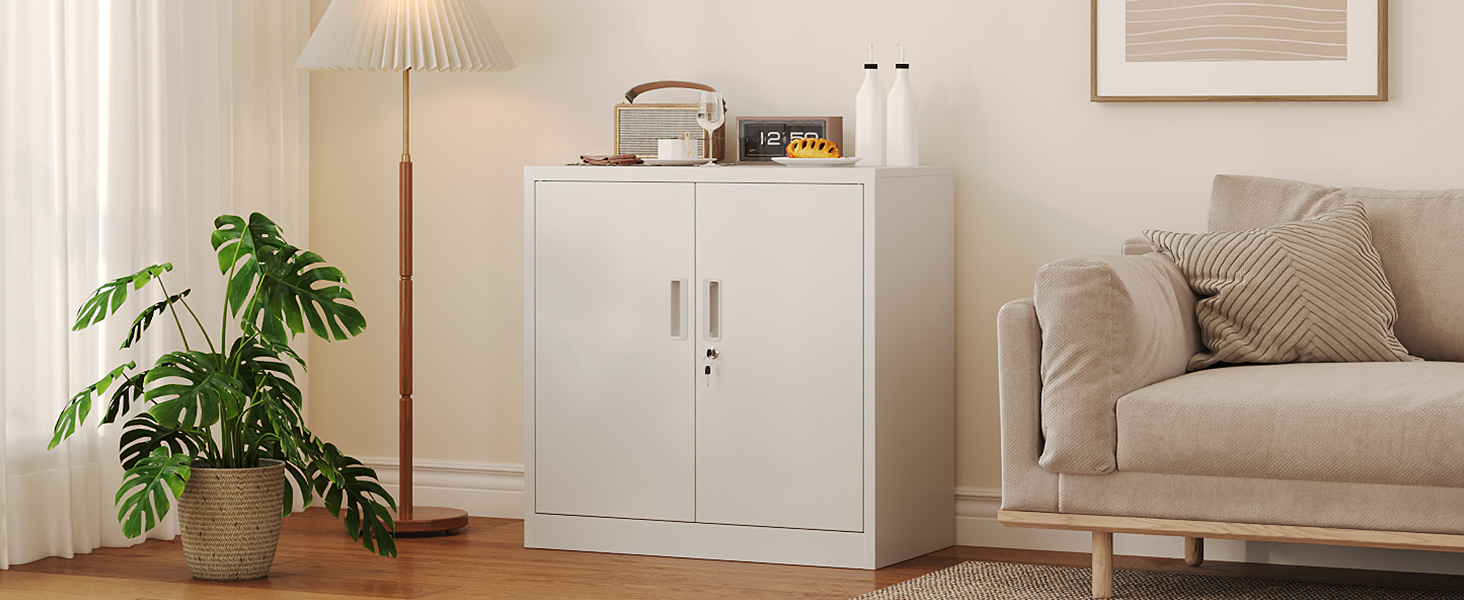 Armoire de rangement blanche à double porte positionnée contre un mur, à côté d'un canapé beige. Plante en pot visible dans un coin. Décoration intérieure moderne et minimaliste.