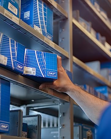 Warehouse shelves stocked with blue SKF product boxes. A hand reaches to retrieve a box, showcasing inventory management in an industrial setting.