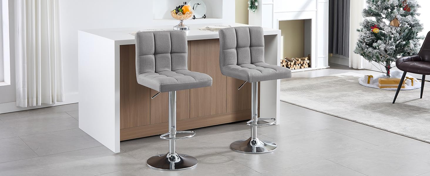 Dos taburetes de bar tapizados en gris con bases cromadas colocados en una moderna encimera de cocina o área de bar blanca