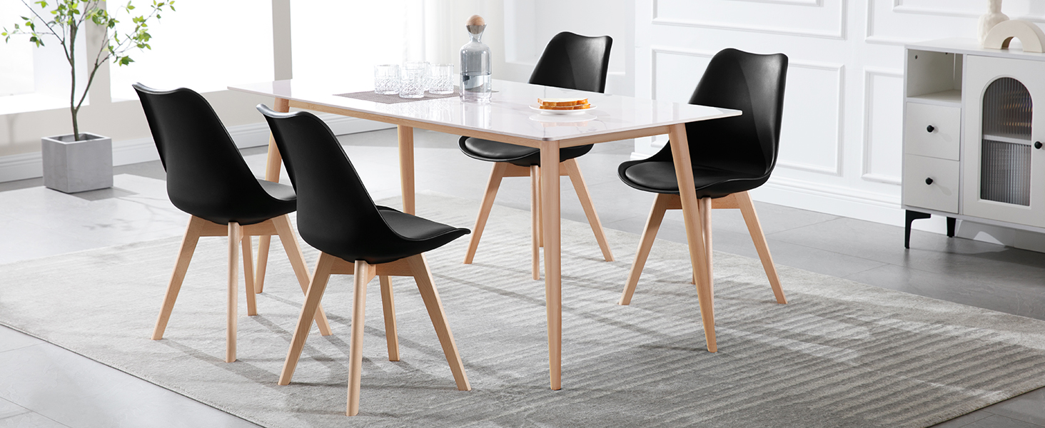 Modern dining set featuring white rectangular table with wooden legs and four black cushioned chairs in contemporary white interior setting.