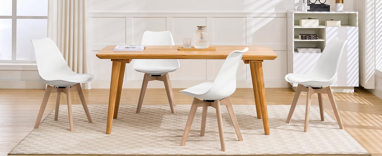 Juego de comedor moderno con mesa de madera y cuatro sillas blancas. La mesa tiene patas cónicas. La habitación incluye estanterías empotradas y una ventana grande, lo que sugiere un diseño interior contemporáneo.