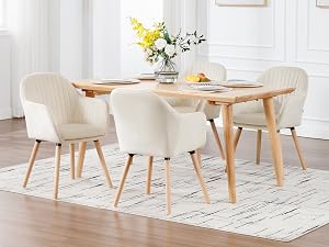 Modern dining set with wooden table and four cream-colored upholstered chairs on geometric patterned rug. White room with decorative wall art and floral centerpiece.
