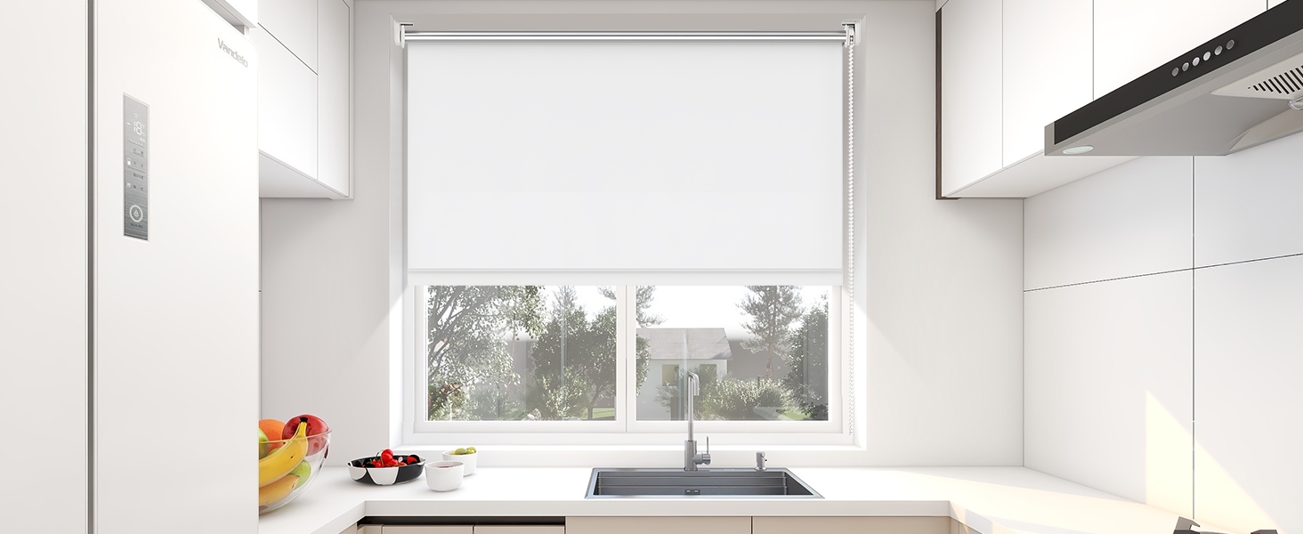 Intérieur de cuisine blanc moderne avec armoires blanches, design minimaliste, store enrouleur blanc sur la fenêtre et évier en acier inoxydable. Des comptoirs propres avec un décor minimal, y compris un bol à fruits coloré