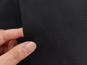 Close-up view of black textured material being pinched between thumb and finger to demonstrate texture or flexibility.