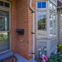 Exterior view of brick building entrance with glass enclosure and small decorative plants near the doorway.