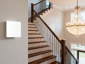 Interior staircase with wooden steps and black metal railings, featuring a crystal chandelier overhead and a white thermostat or control panel mounted on gray wall.