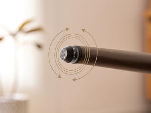 Gros plan d'une buse cylindrique noire ou d'un accessoire muni d'anneaux de mesure circulaires ou de guides marqués sur sa surface, montée sur un fond beige avec un feuillage flou visible.