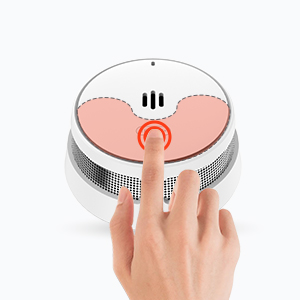 Appareil blanc circulaire avec bouton orange au centre. Une main est montrée en train d'appuyer sur le bouton, ce qui indique qu'il s'agit d'un appareil électronique commandé par l'utilisateur, peut-être pour la domotique ou la sécurité