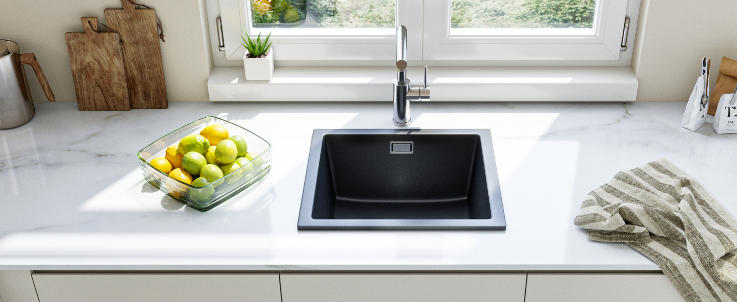 Modern kitchen countertop with white marble surface featuring a black square sink and chrome faucet. A glass bowl of green apples sits nearby.