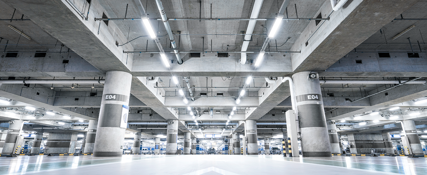 Weitblick auf eine große, gut beleuchtete Tiefgarage oder ein Gebäude. Betonsäulen und Decken mit heller fluoreszierender Beleuchtung sind im gesamten Raum sichtbar