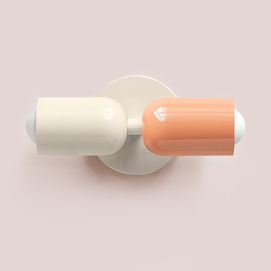 Flacon de vernis à ongles bicolore avec bouchon blanc et moitié inférieure couleur pêche, posé sur le côté sur un fond rose