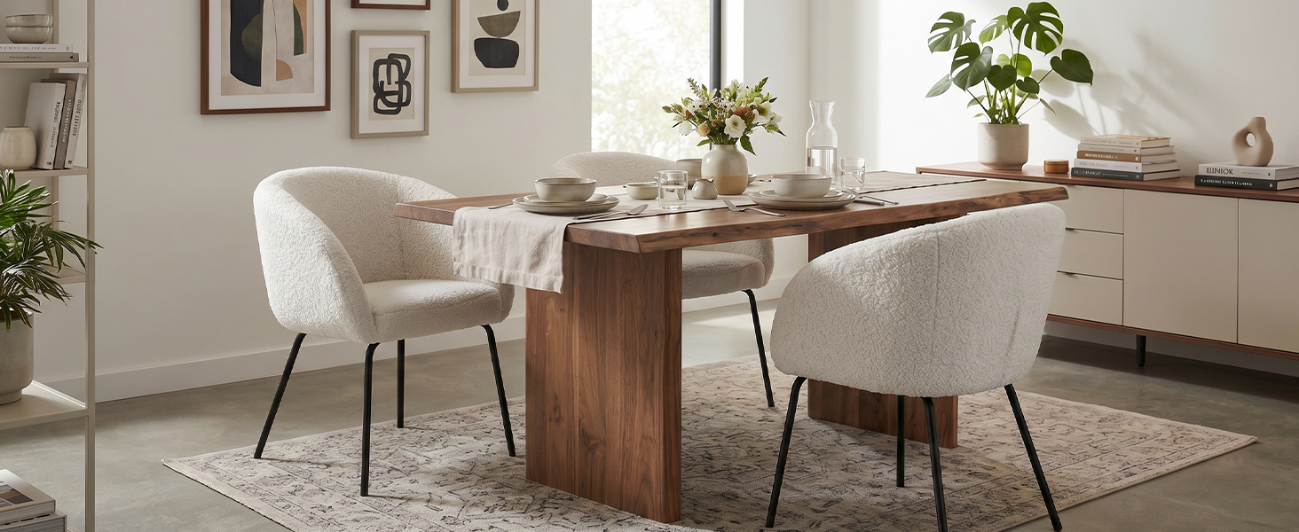 Modern dining room interior with wooden table, white upholstered chairs, potted plants, framed wall art, and neutral décor.