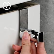 Primer plano de un gancho adhesivo de metal que se instala en una pared, que muestra el proceso de instalación con los dedos presionando el mecanismo de montaje