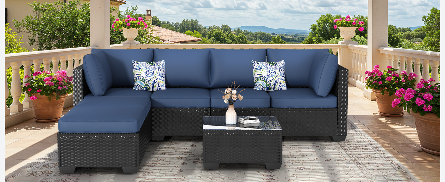 Outdoor sectional patio set with navy blue cushions, including L-shaped sofa, decorative pillows, and dark wicker coffee table on covered terrace.