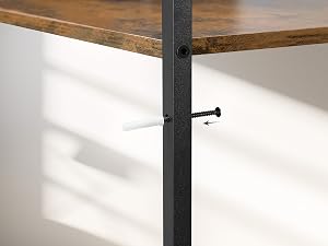 Primo piano di una gamba del tavolo in metallo nero con piedino regolabile, fissata a un piano in legno. La luce del sole proietta ombre su una parete bianca.