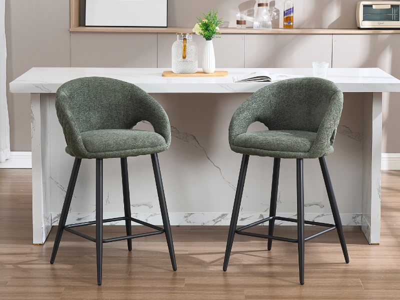 Espacio de comedor moderno con sillas decorativas tapizadas de color verde salvia con patas de metal negro, colocadas en un escritorio o mesa blanca contra el piso de madera.