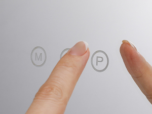 Close-up of two fingers touching a surface with faint circular outlines containing the letters 'M' and 'P'.