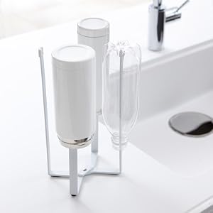 Le texte se lit comme suit : « Image 1 ». Distributeur de savon ou de lotion vertical moderne en plastique blanc monté sur un support en acrylique transparent, placé près du lavabo de la salle de bain avec robinet chromé.