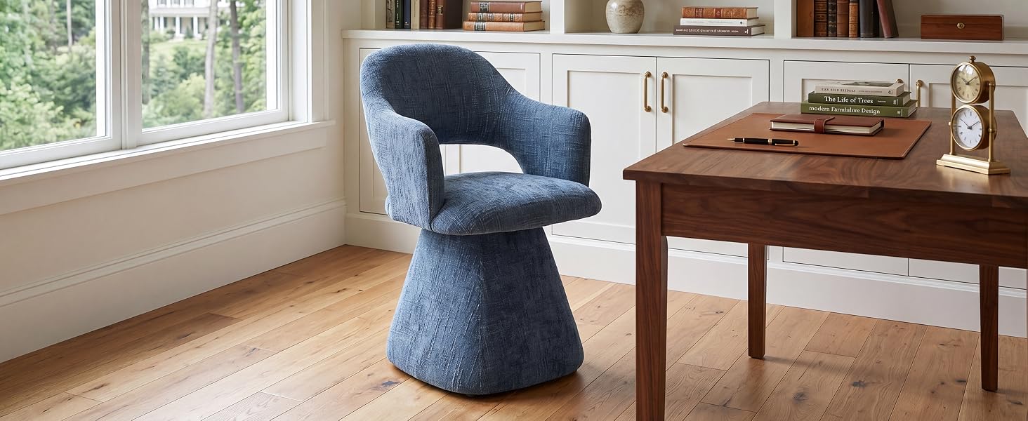 Sedia con piedistallo imbottita blu con schienale curvo esposta in home office accanto alla scrivania in legno vicino alla finestra illuminata dal sole.