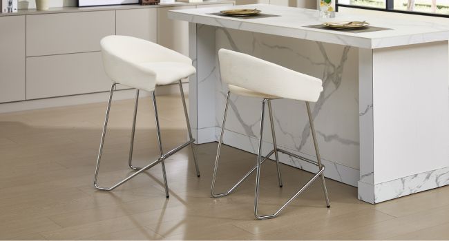 Tabourets de bar blancs modernes à hauteur de comptoir avec des cadres métalliques élégants, placés sur un îlot de cuisine blanc.