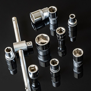 Assortimento di accessori e prolunghe per chiavi a bussola in metallo di varie dimensioni, visualizzati su una superficie scura