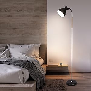 Schwarze Stehlampe mit verstellbarem Kopf in einem minimalistischen Schlafzimmerambiente. Die Lampe beleuchtet den Bereich in der Nähe von Bett und Nachttisch